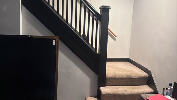 A staircase with a black handrail and beige carpeted steps, a dark-colored door, and a wooden floor. - Tranquil 3-bedroom apartment with AC in Pittsburgh Oakland area. (Pittsburgh)