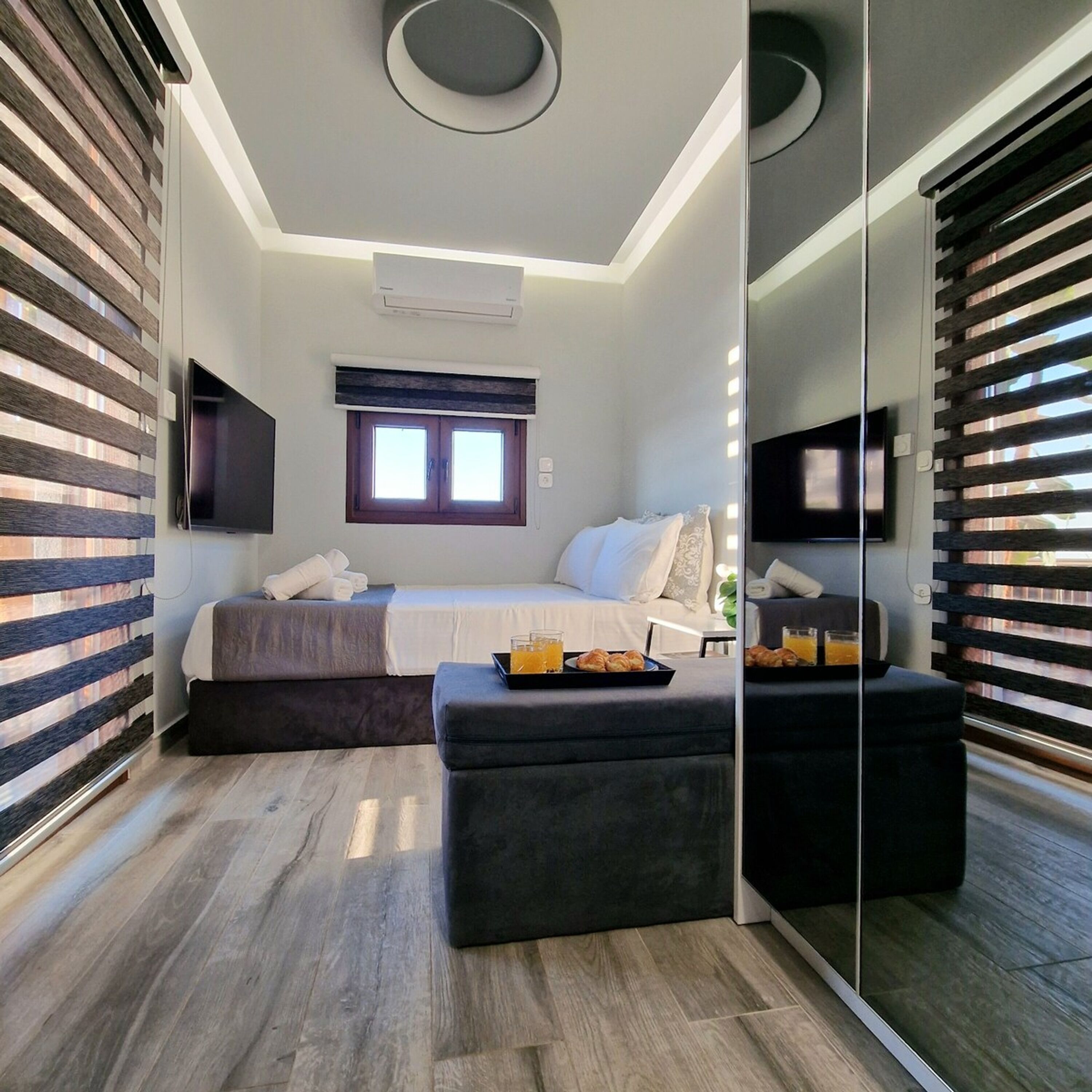 A modern bedroom with a bed, a bedside table with breakfast, a TV, and a large mirror.
