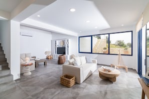 A modern living room with a sofa, coffee table, and a large window with a view of a stone staircase. - Kyma Luxury Villa with private pool (Sivas)