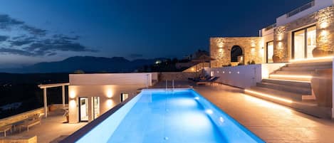 Un área de piscina moderna con un muro de piedra, mobiliario exterior y vistas a las montañas.