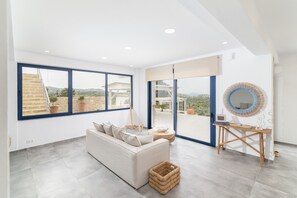 A spacious room with a white sofa, a wooden table, and large windows offering a view of the outdoors. - Kyma Luxury Villa with private pool (Sivas)