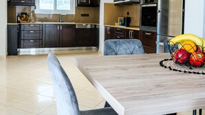 Una cocina moderna con armarios oscuros, electrodomésticos de acero inoxidable y un comedor con mesa de madera y sillas tapizadas en gris.
