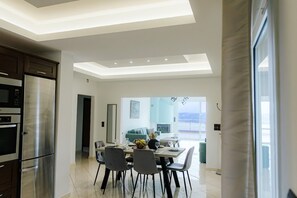 Eine moderne Küche mit Einbauofen und Kühlschrank, ein Essbereich mit Tisch und Stühlen sowie ein Blick in ein Wohnzimmer durch eine offene Tür.