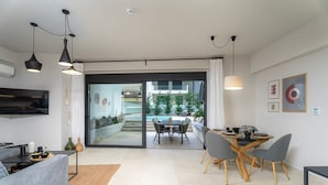 A modern living room with a sofa, dining table, and chairs, a TV, and a view of an outdoor area with a pool. - Speiō Luxury House with private pool (Iraklio)