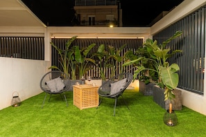 Eine moderne Terrassenanlage mit Kunstgrashalm, zwei Korbstühlen, einem Holztisch und Blumentöpfen.