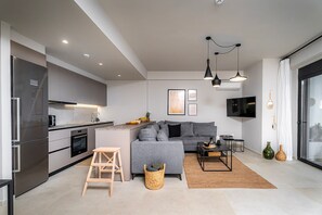 Une cuisine moderne avec un canapé gris, un petit coin repas et un téléviseur fixé au mur.