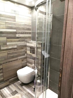 Een moderne badkamer met een douchecabine, toilet en een houten vloer.