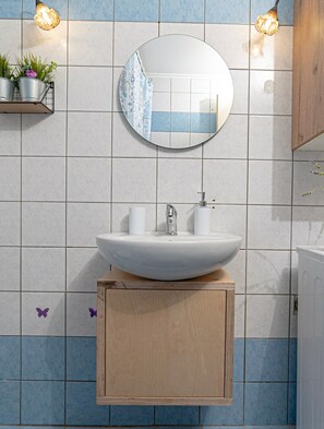 Une salle de bain avec un miroir rond, un lavabo sur colonne blanc et un meuble en bois en dessous.