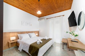 A hotel room with a wooden ceiling, a bed with white linens, a bedside table with a lamp, a small wooden bench, and a wall-mounted TV. - Elva Luxury Villa with private pool (Elea)