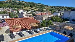 A rooftop pool with lounge chairs and umbrellas, surrounded by stone buildings and a hillside view. - Villa 4 season: Poolside Paradise in Crete (Agia Varvara)