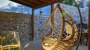 A wicker hanging chair with a cushion, a glass of white wine, and a stone wall in the background. - Villa 4 season: Poolside Paradise in Crete (Agia Varvara)