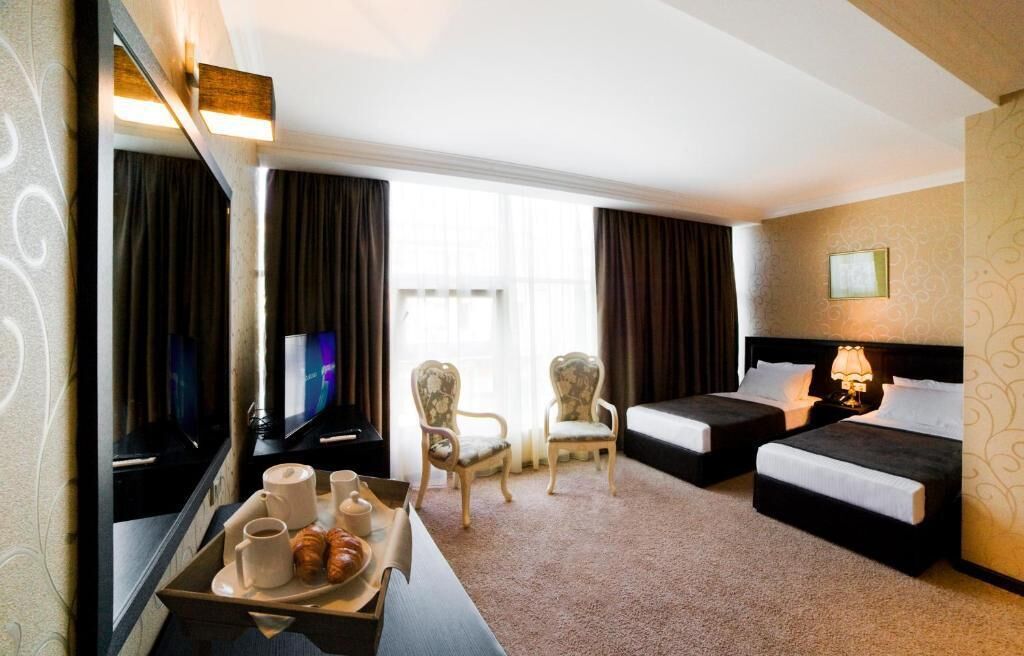 A hotel room with two beds, a desk with a tray of croissants, a coffee machine, and a television.