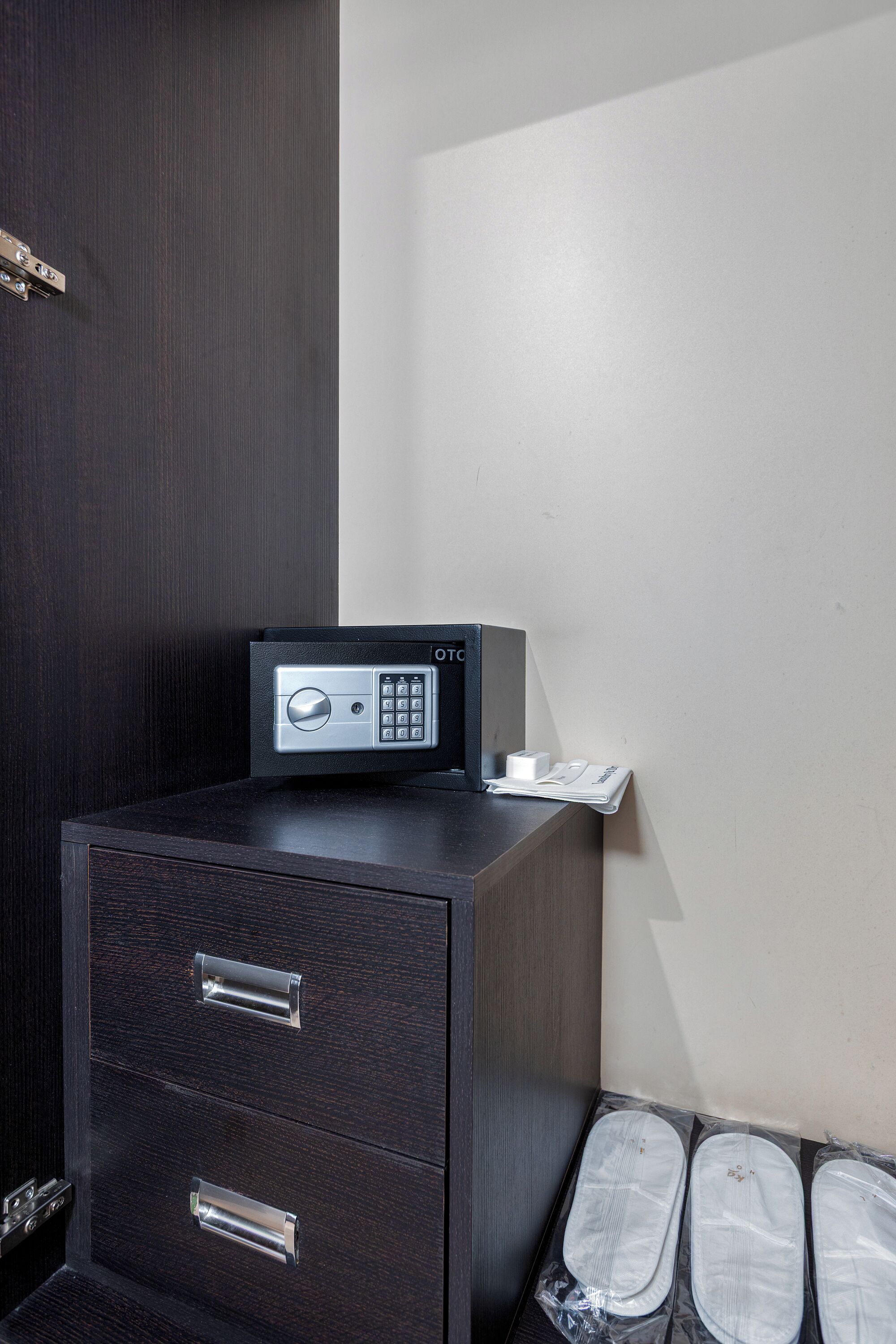 A dark wooden cabinet with a built-in safe, a small table with a telephone, and a pair of slippers.