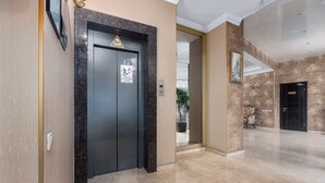 An elevator with a wheelchair accessibility sign, a door with a warning sign, and a marble floor. - Kalasi Hotel (Tbilisi)
