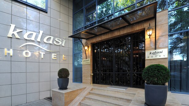 A hotel entrance with a sign reading 'kalasi HOTEL,' a black wrought iron gate, and two potted plants on the steps. - Kalasi Hotel (Tbilisi)