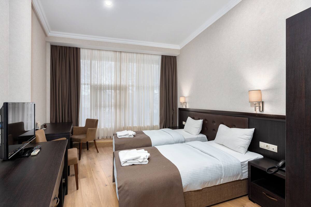 A hotel room with two beds, a desk with a TV, a chair, a lamp, and a bedside table with a phone.