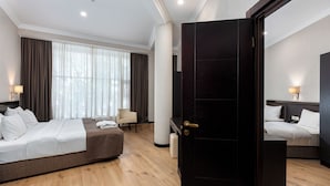 A hotel room with two beds, a sitting area, a large window with curtains, and a dark wooden door. - Kalasi Hotel (Tbilisi)