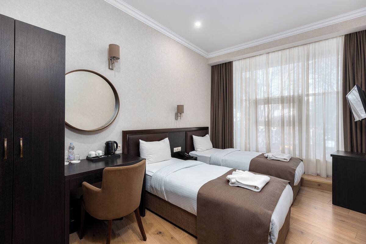 A hotel room with two beds, a desk, a chair, a mirror, and a TV.