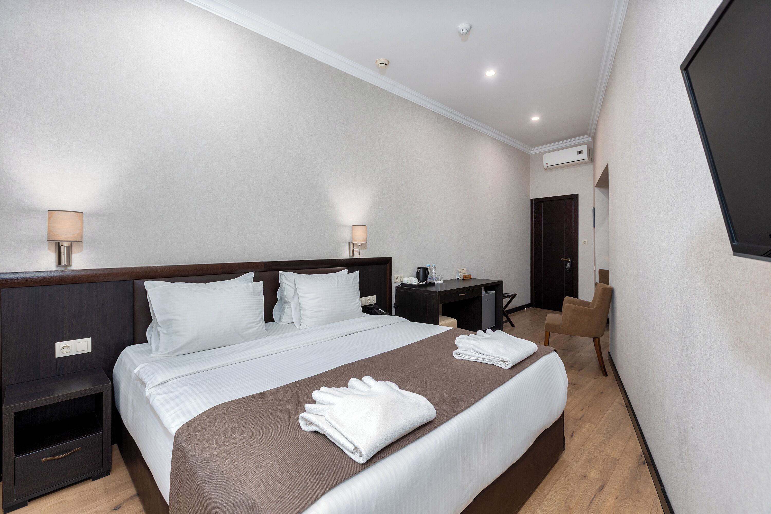 A hotel room with a bed, bedside tables, a desk, and a chair.