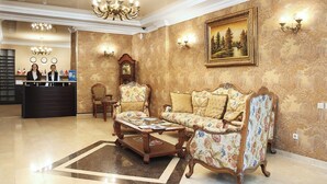 A lobby with a reception desk, two armchairs, a coffee table, a clock, and a painting on the wall. - Kalasi Hotel (Tbilisi)