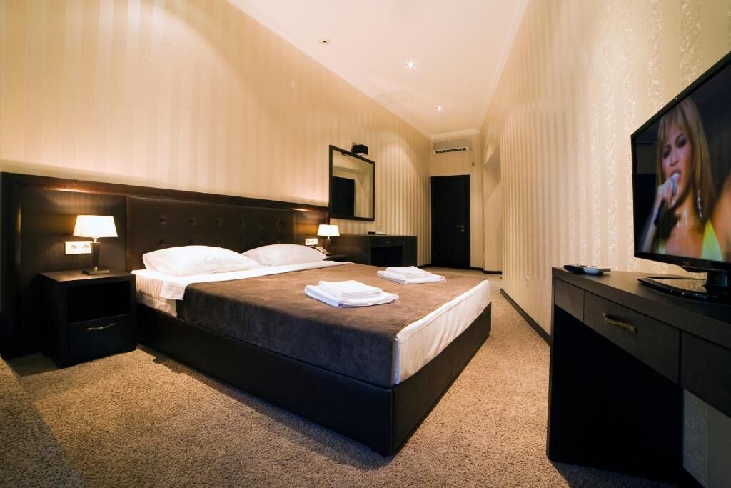 Habitación de hotel con una cama grande, dos mesitas de noche con lámparas, un televisor de pantalla plana y un espejo en la pared.