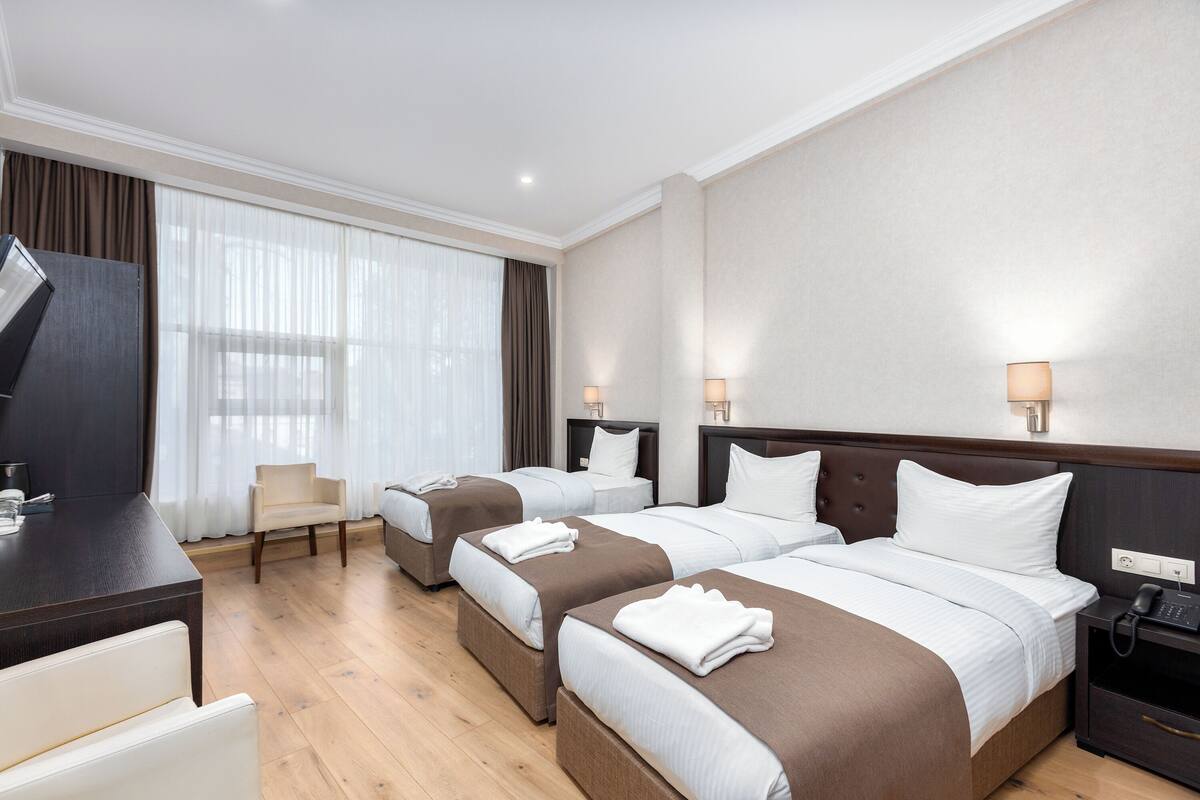 A hotel room with three beds, a desk, a chair, and a phone on the nightstand.