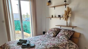 Ein Schlafzimmer mit Bett, Vorhängen, Blick durch eine Schiebetür und Regalen an der Wand.