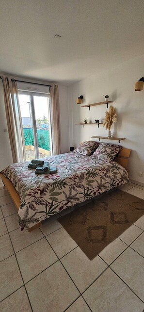 Ein Schlafzimmer mit Bett, Vorhängen, Blick durch eine Schiebetür und Regalen an der Wand.