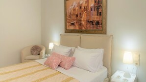 Una habitación de hotel con cama, una silla, una mesita de noche, una lámpara y un cuadro en la pared.
