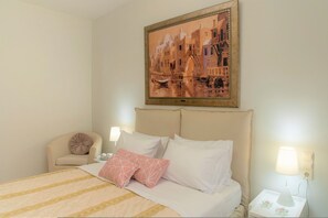Ein Hotelzimmer mit einem Bett, einem Sessel, einem Nachttisch, einer Lampe und einem Bild an der Wand.