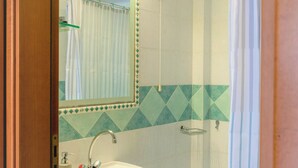 Un baño con lavamanos, espejo, ducha y toallero.