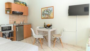 Una cucina compatta con forno a microonde, macchina del caffè e frigorifero, un tavolo da pranzo con sedie e un televisore a schermo piatto montato a parete.