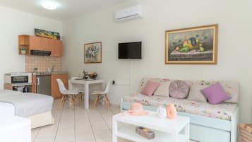 Una habitación moderna y bien iluminada con kitchenette, comedor, sofá y televisor montado en la pared.