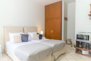 Ein Doppelbett mit gestreifter Bettdecke, ein Nachttisch mit Lampe, ein Holzschrank, eine Mikrowelle und eine Kaffeemaschine auf einem Regal.