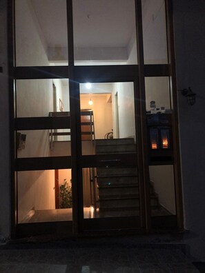 Un interior moderno con una escalera que conduce a un nivel superior, una puerta visible y un accesorio de iluminación fijado a la pared.
