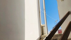 Una scala conduce a una stanza con una finestra, un soffitto con pannelli in metallo ondulato e una piccola presa elettrica sulla parete.