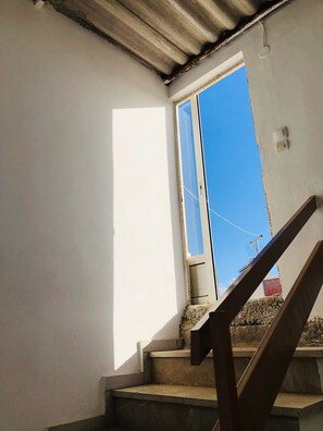 A staircase leading to a room with a window, a ceiling with a corrugated metal section, and a small electrical outlet on the wall. - Ariadni's apartment 3 (Chania)