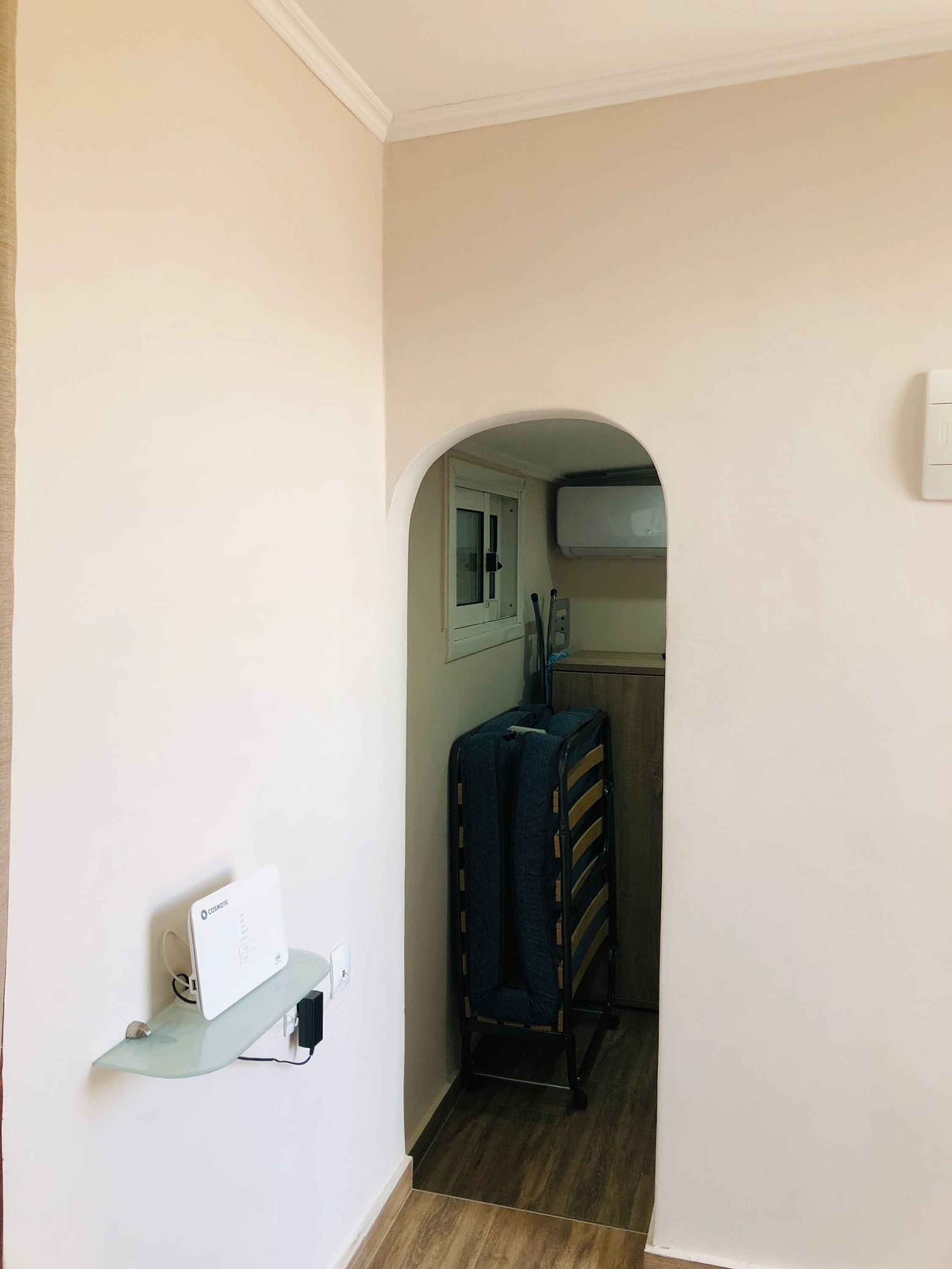 A hallway with a white wall, a glass shelf with a device, a blue suitcase, and a wooden cabinet.