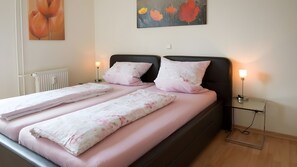 Un letto rifatto con cura, lenzuola rosa, una testiera nera e due abat-jour.