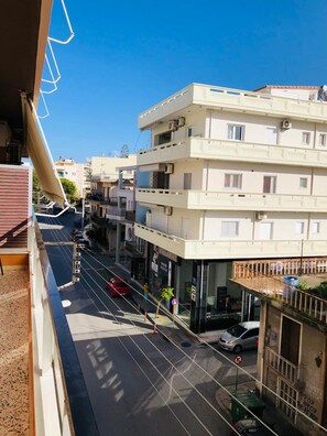 Un immeuble à plusieurs étages doté de balcons, une rue bordée de voitures et un ciel bleu dégagé.