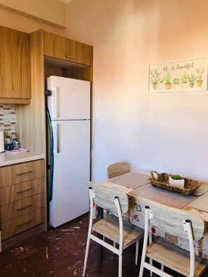 Eine kleine Küche mit Holzschränken, einem weißen Kühlschrank, einem Esstisch mit Stühlen und einem Wandbild.