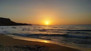 Ein Strand mit Wellen, einem Sonnenuntergang und fernen Bergen.