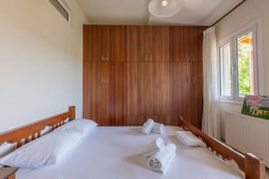 Ein Schlafzimmer mit einem Holzschrank, einem Bett mit weißer Bettwäsche und einem Fenster mit Blick ins Grüne.