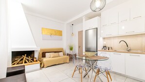 Ein modernes Wohnzimmer mit einer Couch, einem Glastisch und einer Küchenzeile mit weißen Schränken und einem Edelstahlkühlschrank.