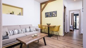 Ein Wohnzimmer mit Sofa, Couchtisch, Esstisch mit Stühlen und einem Flur, der zu einem Schlafzimmer führt.