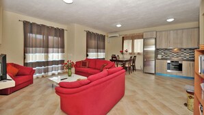 Ein Wohnzimmer mit roten Sofas, einem Esstisch und einer Küchenzeile mit modernen Geräten.