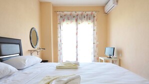 Ein Hotelzimmer mit Bett, Nachttisch mit Fernseher, Spiegel und Fenster mit blumigem Vorhang.