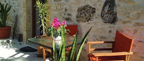 A stone building with a table and chairs, potted plants, and a door.
