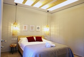 Une chambre à coucher avec un lit, deux lampes suspendues, une petite table de chevet en bois et une porte.