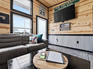 A cozy room with a couch, a round coffee table with a book and a notepad, a wall-mounted TV, and a speed limit sign.
